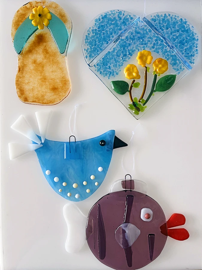 A collection of colorful, whimsical glass art pieces featuring a flip-flop, a bird, a fish, and a whimsical round a heart, made at the Glass Duchess Studio in Port Charlotte, FL